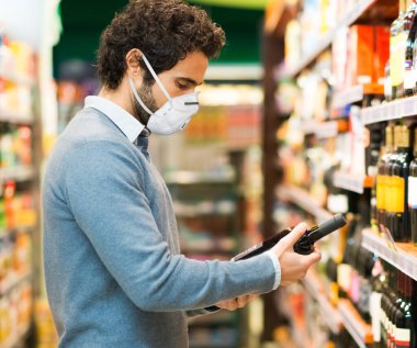 Süpermarkette Coronavirus salgını sırasında şarap şişesi seçen bir adam.