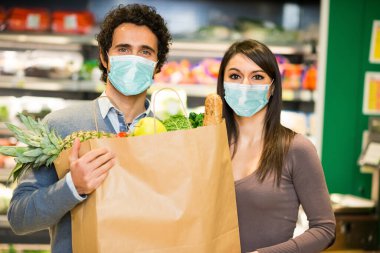 Koronavirüs salgını sırasında süpermarkette yiyecek dolu bir çanta tutan maskeli çift.