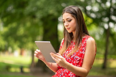 Parkta dijital tablet kullanan genç bir kadın.