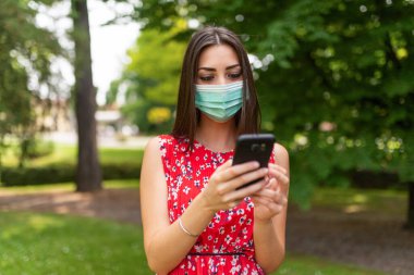 Cep telefonunu kullanan maskeli genç bir kadın.