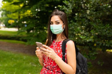 Cep telefonunu kullanan maskeli genç bir kadın.