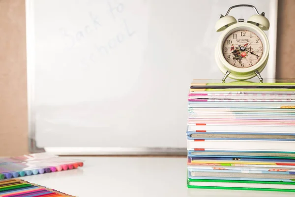 Mesa branca com pilha de livros coloridos, despertador e material escolar, espaço de cópia, tempo de estudo em casa para crianças — Fotografia de Stock