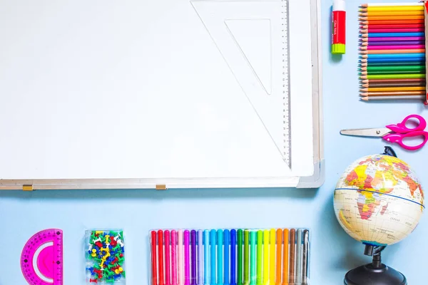 Schulbedarfskonzept für die Grundschule - Globus, Farbstifte und Bleistifte, Klebestift, Schere, Stecknadeln, Lineale auf blauem Hintergrund mit weißer Tafel. — Stockfoto