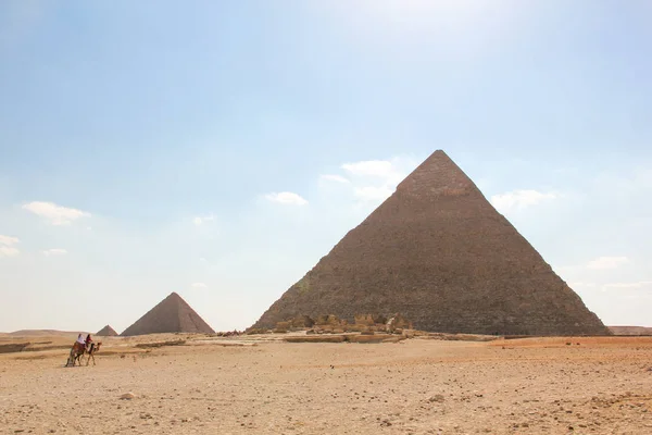 Blick aus der Wüste auf eine Reihe von Pyramiden, die drei Pyramiden des Giza-Komplexes mit marschierenden Reitern — Stockfoto