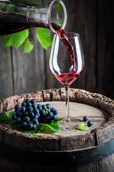 Despejando vinho tinto da garrafa em um copo no barril velho — Fotografia de Stock