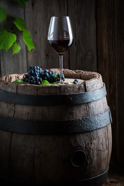 Glas Rotwein und Trauben auf altem Holzfass — Stockfoto