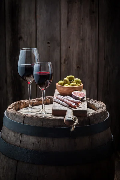 Tasty red wine in glass with olives and cold meats on wooden barrel — Stock Photo, Image