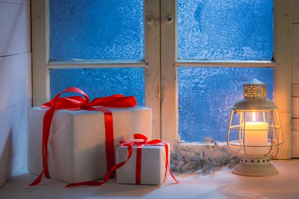 Cadeaus voor kerst met een bevroren venster en kaarslicht 's nachts — Stockfoto