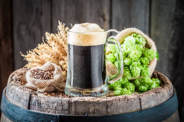 Pint of dark beer with wheat and hops on barrel — Stock Photo, Image