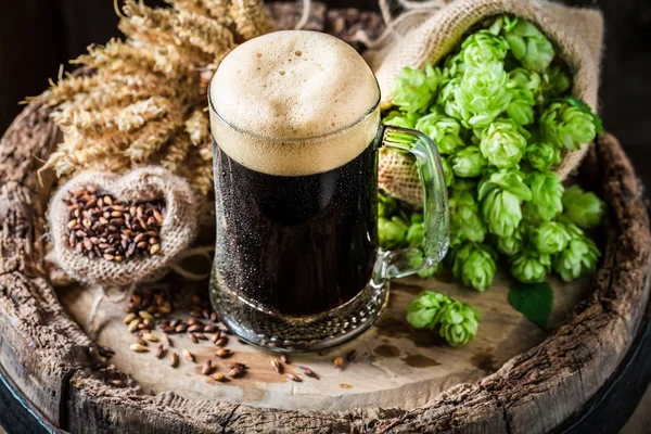 Dark beer with foam, wheat and hops on oak barrel — Stock Photo, Image