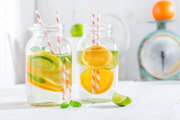 Agua con cítricos y hojas de menta sobre una mesa blanca —  Fotos de Stock