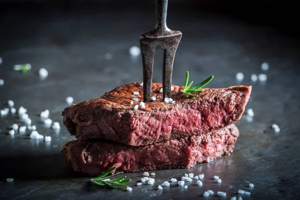 Closeup of medium rare steak with rosemary on metal table