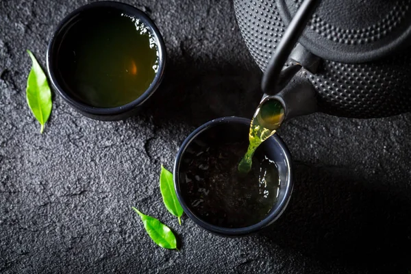 Grüner Tee in Tasse auf schwarzem Felsen gießen — Stockfoto