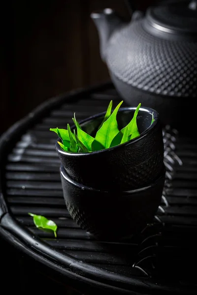 Folhas de chá verde em xícara de chá sobre fundo preto — Fotografia de Stock