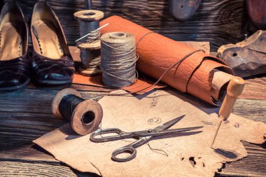 Closeup of tools, shoes and leather in cobbler workshop clipart