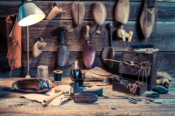 Taller con zapatos, herramientas y cuero sobre mesa de madera — Foto de Stock