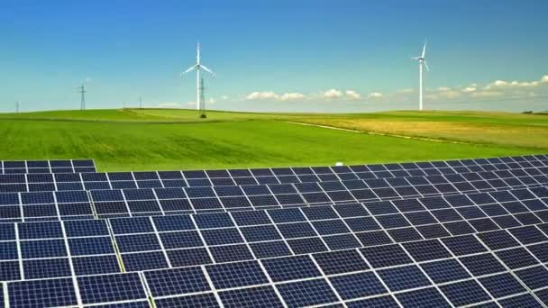 Солнечные панели и ветряные турбины на зеленом поле, вид с воздуха — стоковое видео