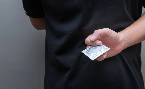 Fechar a mão de um jovem, segurando o preservativo atrás das costas — Fotografia de Stock