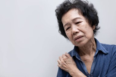 Elderly Asian woman put her hand on his shoulder because of shoulder pain or muscle pain. Healthcare and Medical concept clipart