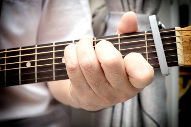 Akustik gitarın perdesine yerleştirilmiş erkek parmaklarını kapat