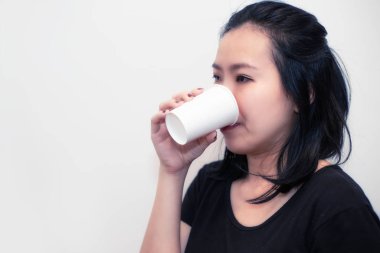 Asyalı genç bir kadın beyaz bir bardak su ya da başka bir içecek içiyor.