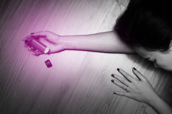 Woman lying on the ground with holding a pressurized cartridge inhaler extended pharynx, Bronchodilator. Emergency concept. Black and white tone and red spot on her hand