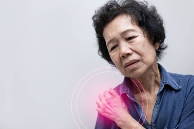 Elderly Asian woman put her hand on her shoulder because of shoulder pain or muscle pain, with red spot on her shoulder. Healthcare and Medical concept clipart