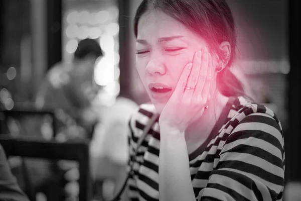 Beautiful Asian woman touched her cheek with painful expression because of suffering from toothache. Soft focus with black and white tone and red spot on her cheek