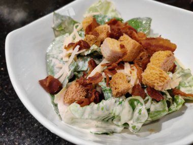 Marullu Sezar salatası, kızarmış pastırma ve parmesan peyniri. Beyaz seramik kasede servis ediliyor.