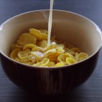 Milk is pouring in Corn Flakes on wooden background