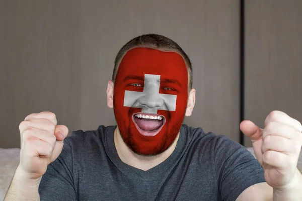 Face of young screaming  man painted with flag of Switzerland. Soccer team fan.