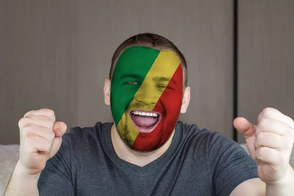 Face of young screaming man painted with flag of Congo. Soccer team fan.