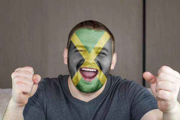 Face of young screaming man painted with flag of Jamaica. Soccer team fan.