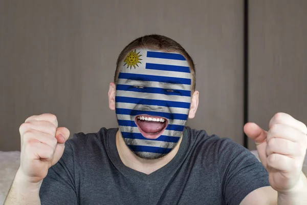 Face of young screaming man painted with flag of Uruguay. Soccer team fan.