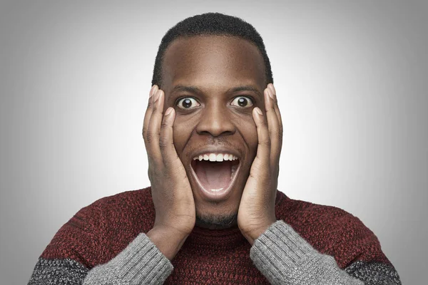 Close-up portret van opgewonden African American man met geschokt en verbaasd gezicht, op zoek en schreeuwen bij camera met grote ogen en mond wijd open, bedrijf handen op zijn wangen. Wow gezicht concept. — Stockfoto