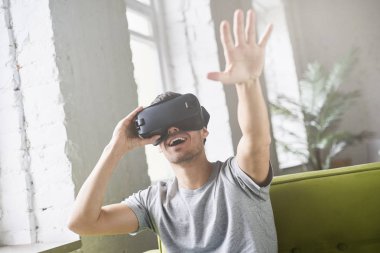 Sanal gerçeklik evde kanepede oturan ve havada, el atma Vr kulaklık, gözlükle yaşandığı Hansome Avrupa erkek el hareketi. Giyen yuvarlak pencere ya da video oyunları oynarken gözlük genç adam