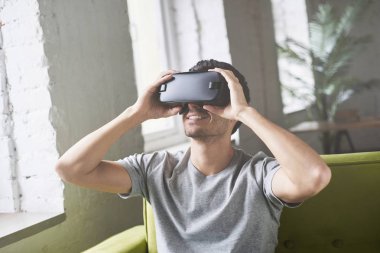 Teknolojisi, oyun ve insanlar kavramı. Video oyun oynarken veya yeşil kanepeye evde oturup film izlerken holding sanal gerçeklik kulaklık veya 3d gözlük, gri tişört, genç çekici beyaz adam