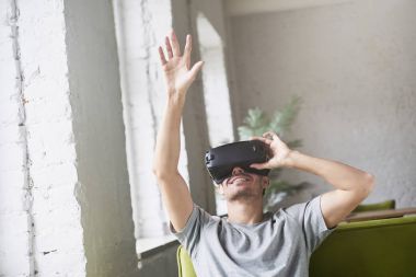 Havada bir şey genç beyaz erkek top tutmaca oynamak için mobil oyun uygulamaları, evde koltukta oturan yenilikçi sanal gerçeklik kulaklık. Mobil Oyunlar apps ile yenilikçi gözlük kullanın.