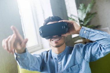 Yakışıklı adam portresi closeup gömlek, modern coworking studio, sanal gerçeklik gözlük takan bir şey ile etkileşim sanki parmak ile işaret dedim. Gelecek şu andır. VR teknolojisi kullanarak