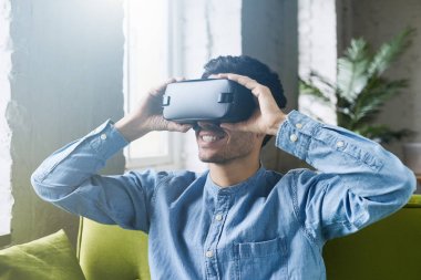 VR mezartaşı ile kullanılarak akıllı telefon. Yuvarlak pencere yarığı kulaklık üzerinde elele, sanal gerçeklik waching film veya video oyunu oynarken yaşandığı hayretler içinde genç beyaz erkek. Lens etkisi fişekleri