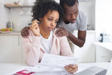 Afro-Amerikan erkek ödenmemiş faturaları online banka uygulamasını kullanarak dizüstü bilgisayar ekranına bakarak destekleyici kocası ile analiz. Genç iflas çift mali sorunları var. Hiçbir para kavramı