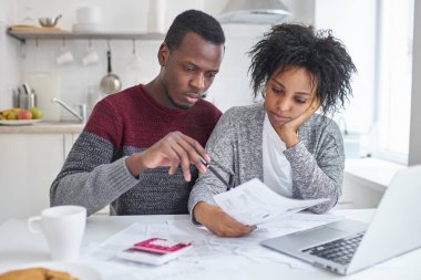 Genç Afrikalı-Amerikalı eşi ve parasız olan dizüstü bilgisayar, hesap makinesi ve evrak birlikte yaptığı, giderleri analiz, Aile bütçe planlama ve faturaları, hesaplama kağıtları evde oturan kocası