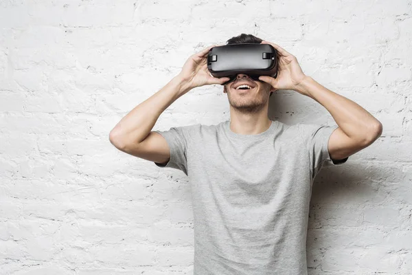 Hansome Avrupa erkek gri t-shirt sanal gerçeklik Vr kulaklık gözlükle yaşıyor. Beyaz delikanlı yuvarlak pencere ya da iskambil video spor, beyaz duvara karşı ayakta gözlük