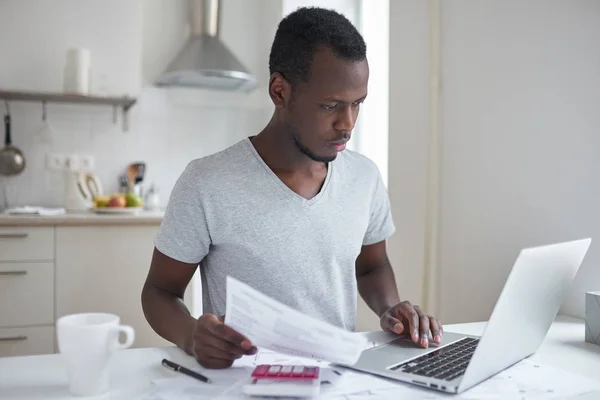 Geconcentreerde jonge Afrikaanse Amerikaanse student met behulp van online bankieren toepassing met hand op de touchpad, kijken naar scherm van zijn laptop, proberen te maken van de betaling voor universitair onderwijs. Financiële problemen — Stockfoto