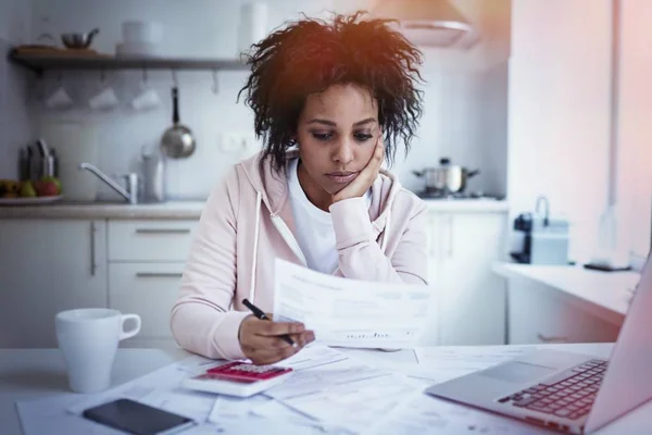 Jovem solteiro chateado afro-americano dona de casa sentado na mesa da cozinha com papéis, laptop e calculadora, tentando fazer ambas as extremidades atender, não tendo dinheiro para pagar dívidas. Conceito de problemas financeiros — Fotografia de Stock