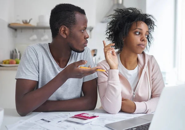 Esposa africana enojada y marido discutiendo sobre problemas financieros graves, sentado en la mesa de la cocina con la calculadora y el ordenador portátil, tratando de hacer el plan de finanzas, teniendo problemas con los pagos. Familia infeliz —  Fotos de Stock