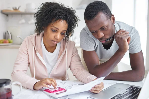 Hangsúlyozta, afro-amerikai házaspár együtt dolgoznak a papírmunka, kiszámítása a kiadások, megpróbálja menteni egy kis pénzt, családi pénzügyek, ülő-on konyhaasztal laptop és számológép irányítása — Stock Fotó