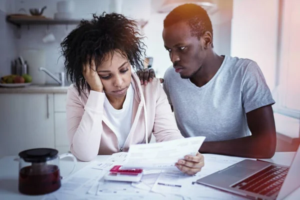 Conceito de problemas financeiros. Jovem afro-americana infeliz e deprimida calculando o orçamento familiar, planejando despesas, tentando fazer com que ambas as extremidades se encontrem. Marido tentando animar sua esposa triste — Fotografia de Stock