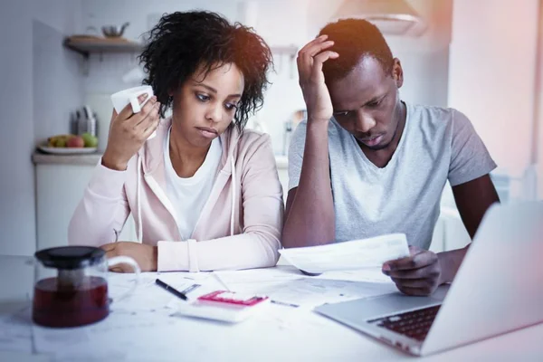 Afro-amerikai házaspár felülvizsgálata pénzügyeik ül a konyhaasztalnál hangsúlyozta: feleség és a férj számítások papírok és laptop. Az emberek és a pénzügyek fogalmát. Családi költségvetés és adósság — Stock Fotó
