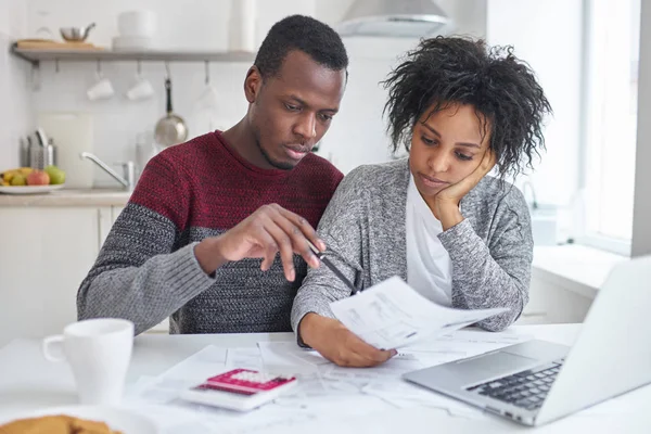 Jonge African American vrouw en man om thuis te zitten met laptop, rekenmachine en papieren papierwerk samen doen, analyseren van de kosten, planning gezinsbudget en berekening van de rekeningen, hebben geen geld — Stockfoto